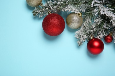 Photo of Christmas balls and fir tree branches with snow on light blue background, flat lay. Space for text