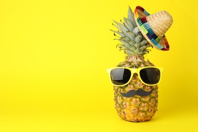 Photo of Pineapple with Mexican sombrero hat, sunglasses and fake mustache on yellow background, space for text