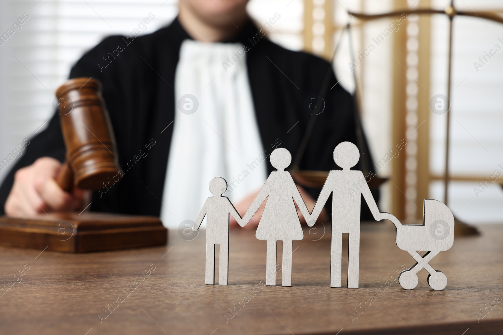 Photo of Family law. Judge with gavel sitting at wooden table, focus on figure of parents and children