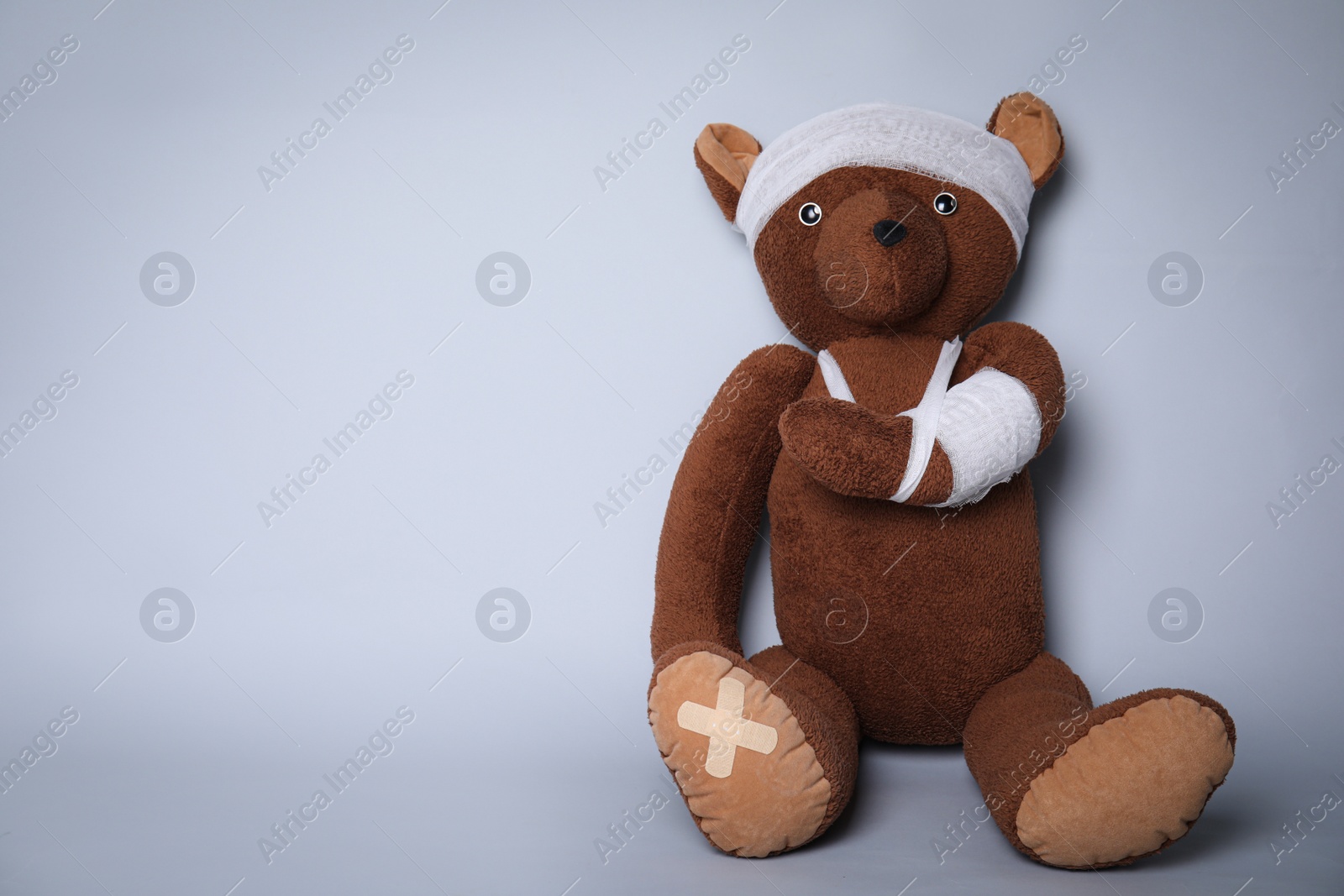 Photo of Toy bear with bandages on light grey background. Space for text