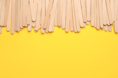 Photo of Wooden waxing spatulas on yellow background, flat lay. Space for text