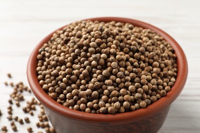 Dried coriander seeds in bowl on light table, closeup