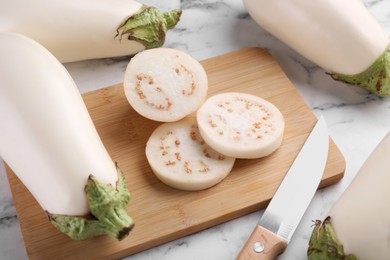 Photo of Wooden board, raw white eggplants and knife on marble table
