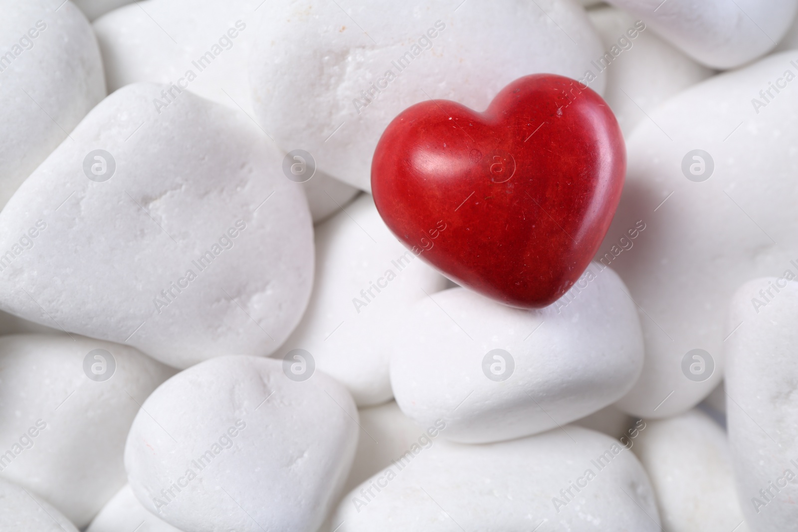 Photo of Decorative heart on white pebble stones, top view