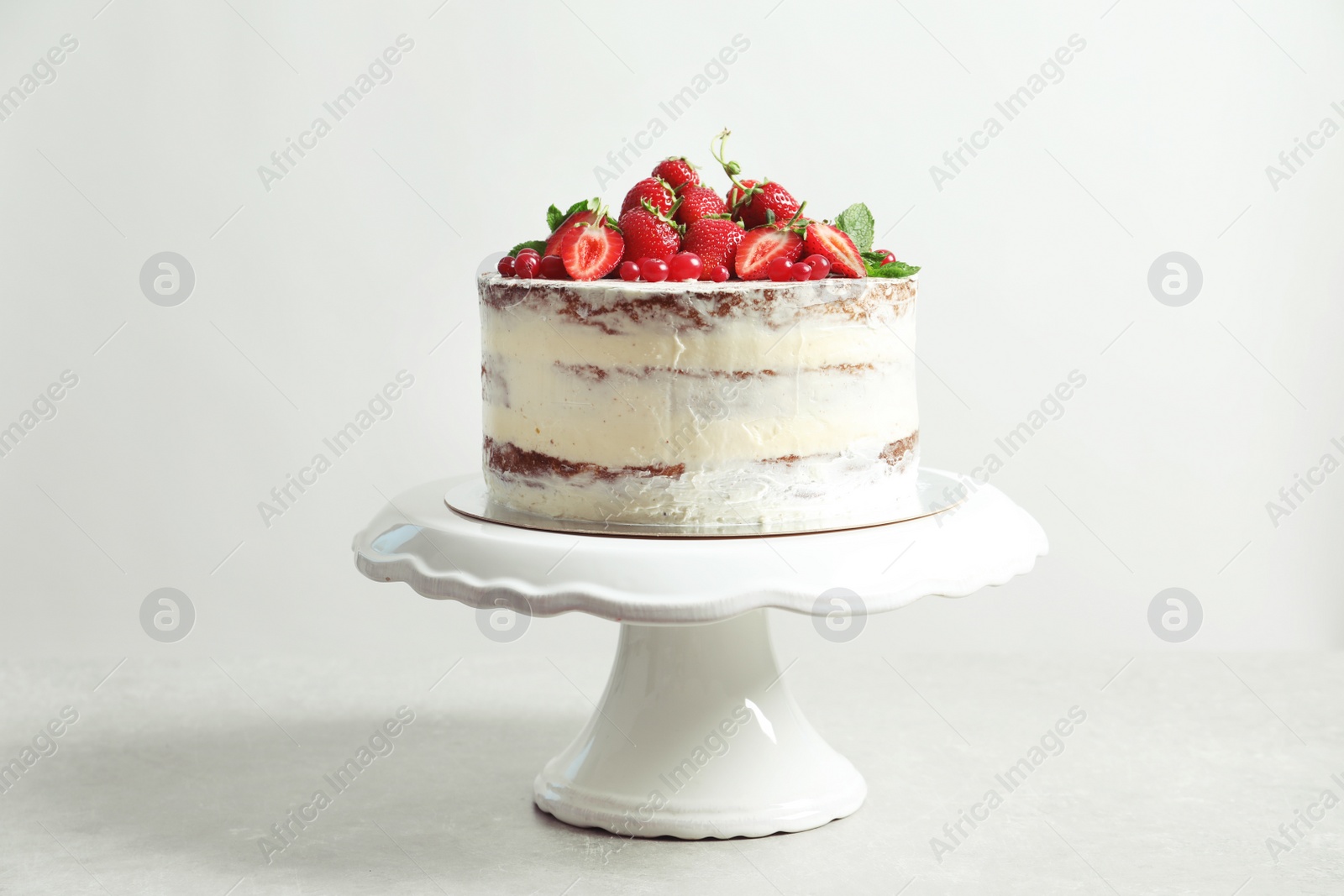 Photo of Delicious homemade cake with fresh berries on stand against light background