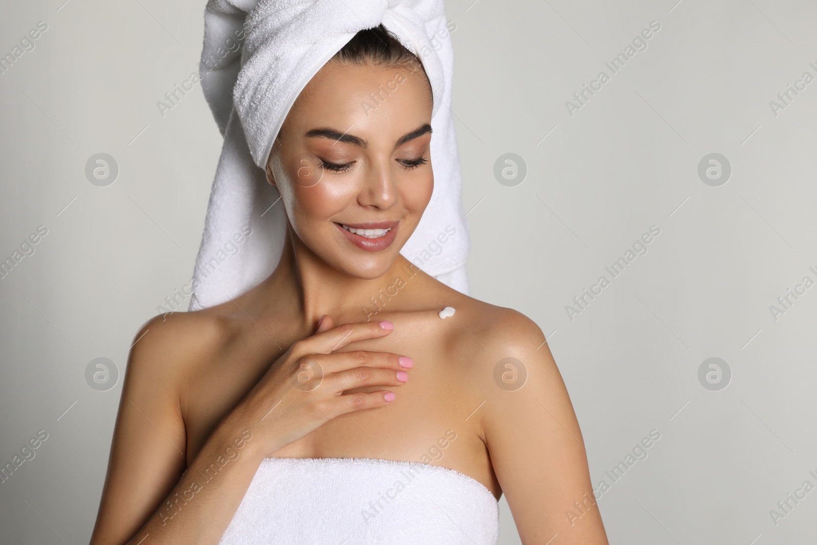 Photo of Beautiful young woman with towels applying cream on shoulder against light background