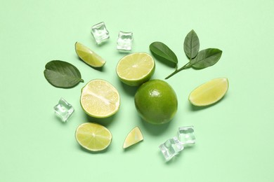 Photo of Fresh ripe limes with leaves and ice cubes on light green background, flat lay