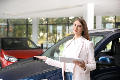 Photo of Woman with tablet in modern car dealership