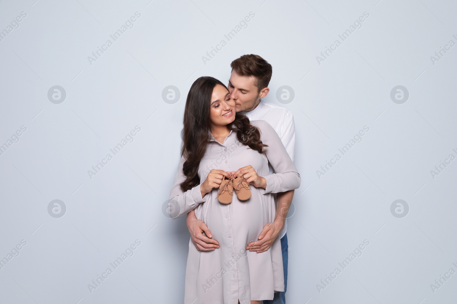 Photo of Pregnant woman and her husband holding little shoes on color background