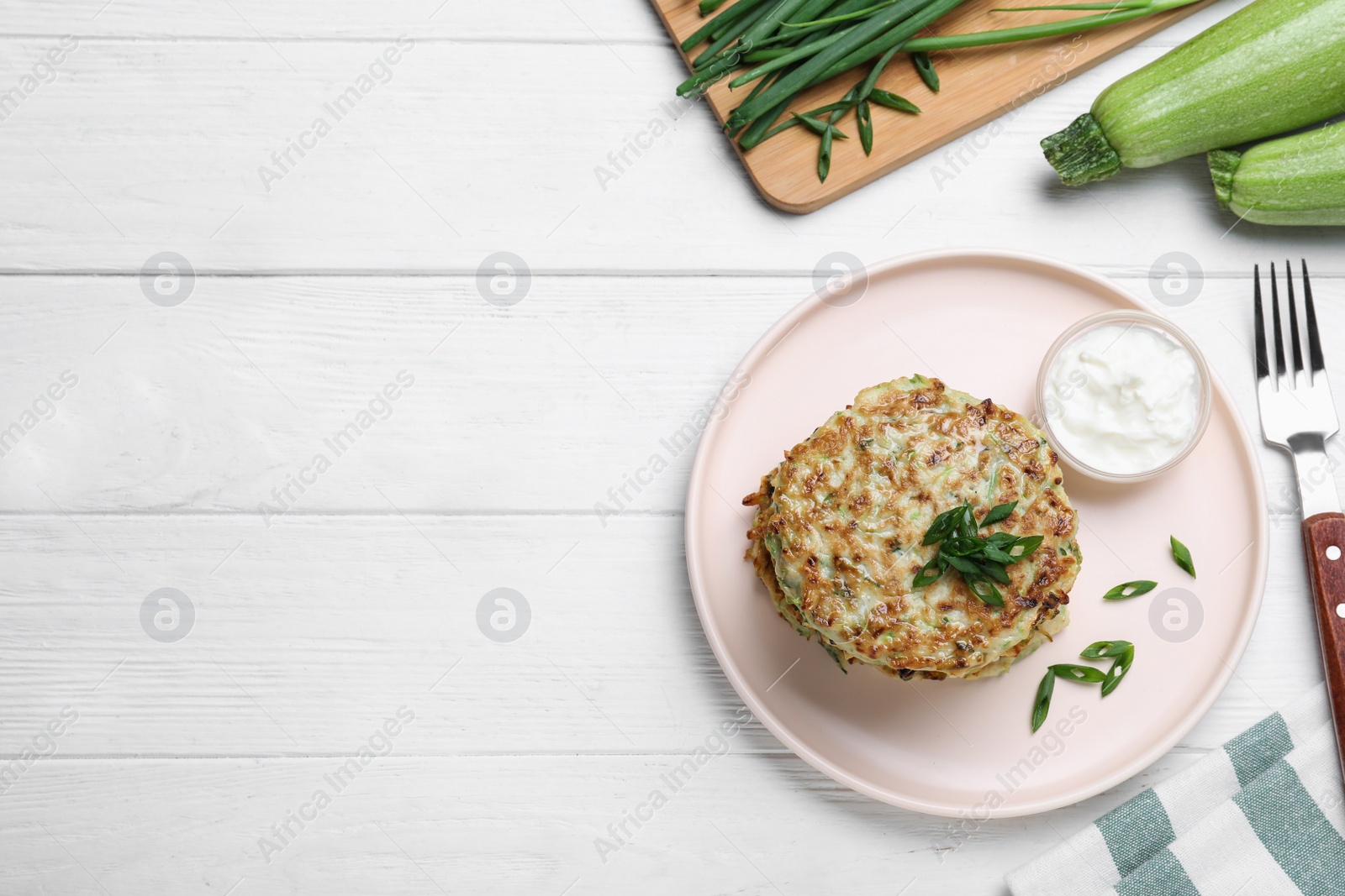 Photo of Delicious zucchini fritters served on white wooden table, flat lay. Space for text