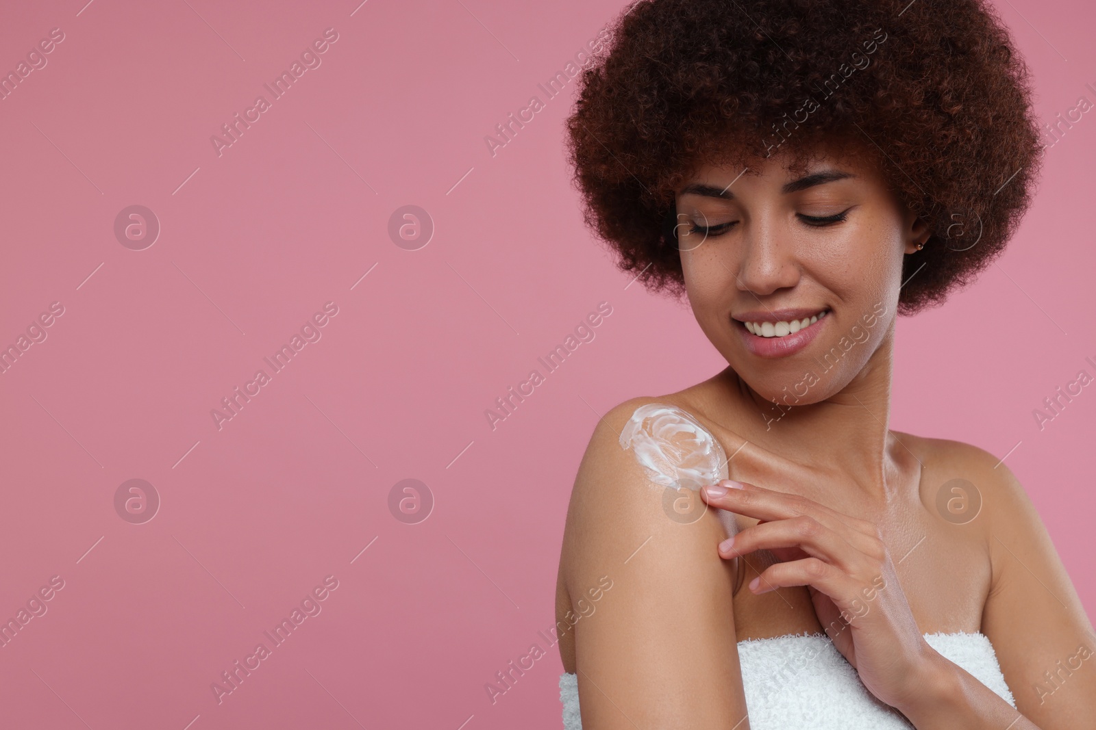 Photo of Beautiful young woman applying body cream onto shoulder on pink background, space for text