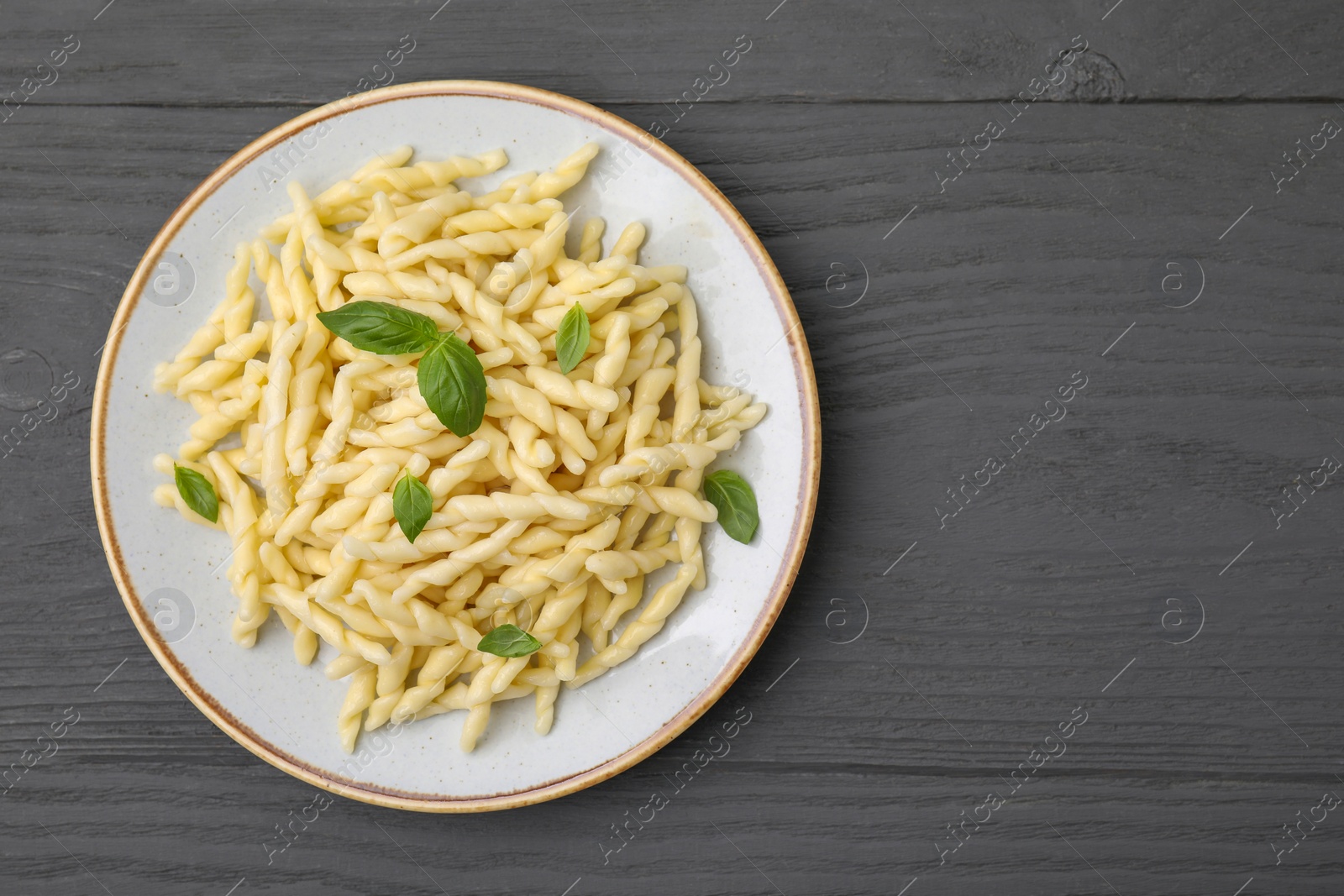 Photo of Plate of delicious trofie pasta with basil leaves on grey wooden table, top view. Space for text