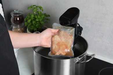 Photo of Woman taking out vacuum packed meat from pot in kitchen, closeup. Thermal immersion circulator for sous vide cooking