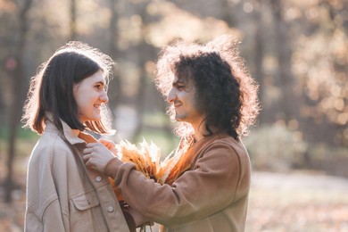 Happy young couple with dry leaves spending time together in autumn park, space for text. Dating agency