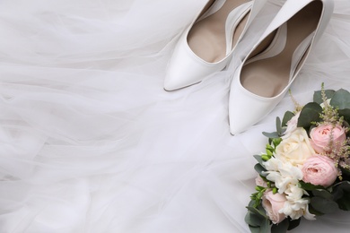 Photo of Pair of wedding high heel shoes and beautiful bouquet on white veil, flat lay. Space for text