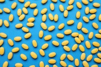 Photo of Many yellow dragee candies on blue background, flat lay