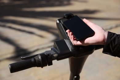 Photo of Man using smartphone to pay and unblock rental electric scooter outdoors, closeup