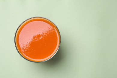 Glass with healthy carrot juice on light green background, top view. Space for text