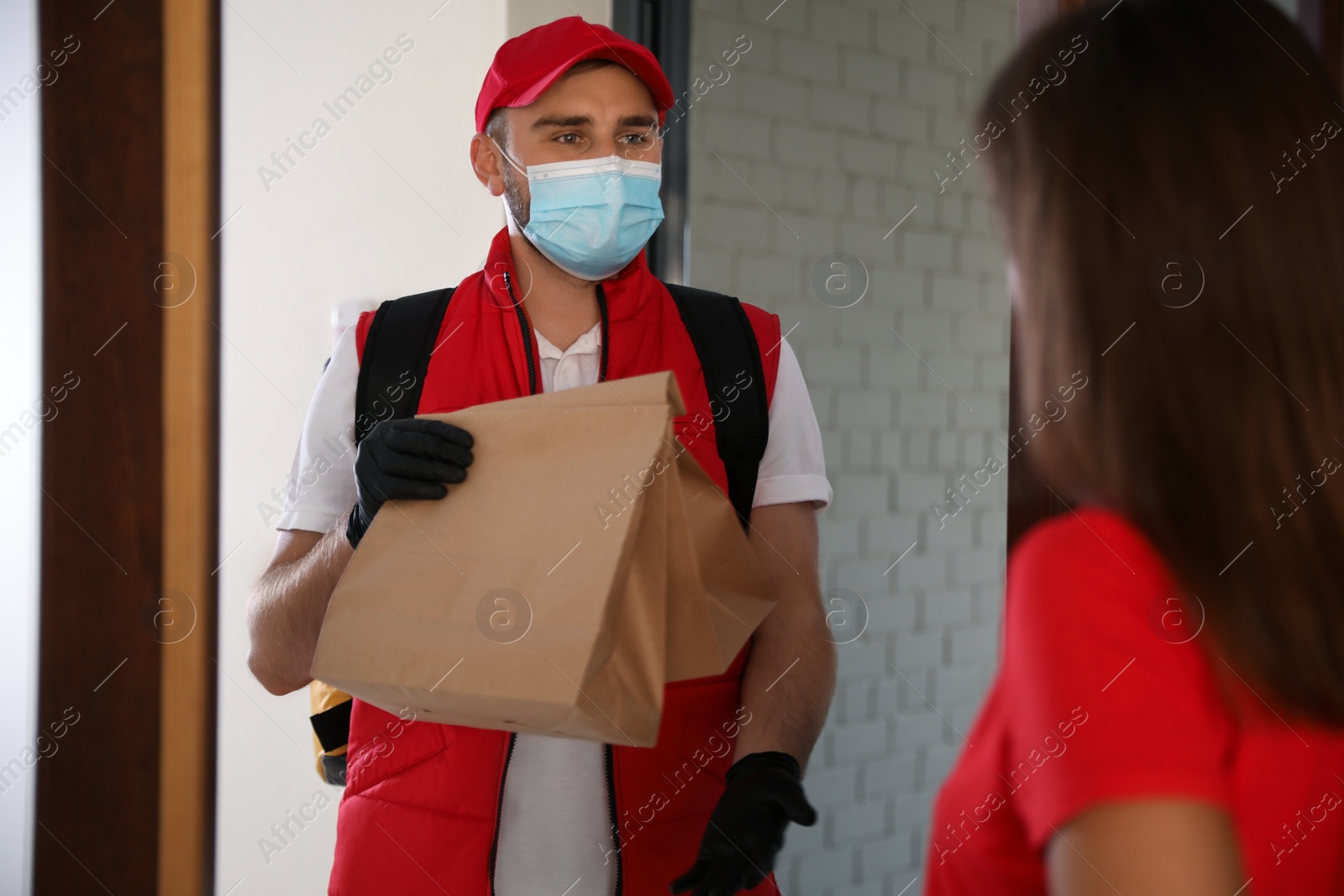 Photo of Courier in protective mask and gloves giving order to woman at entrance. Restaurant delivery service during coronavirus quarantine