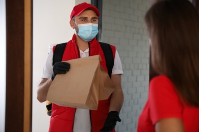 Courier in protective mask and gloves giving order to woman at entrance. Restaurant delivery service during coronavirus quarantine