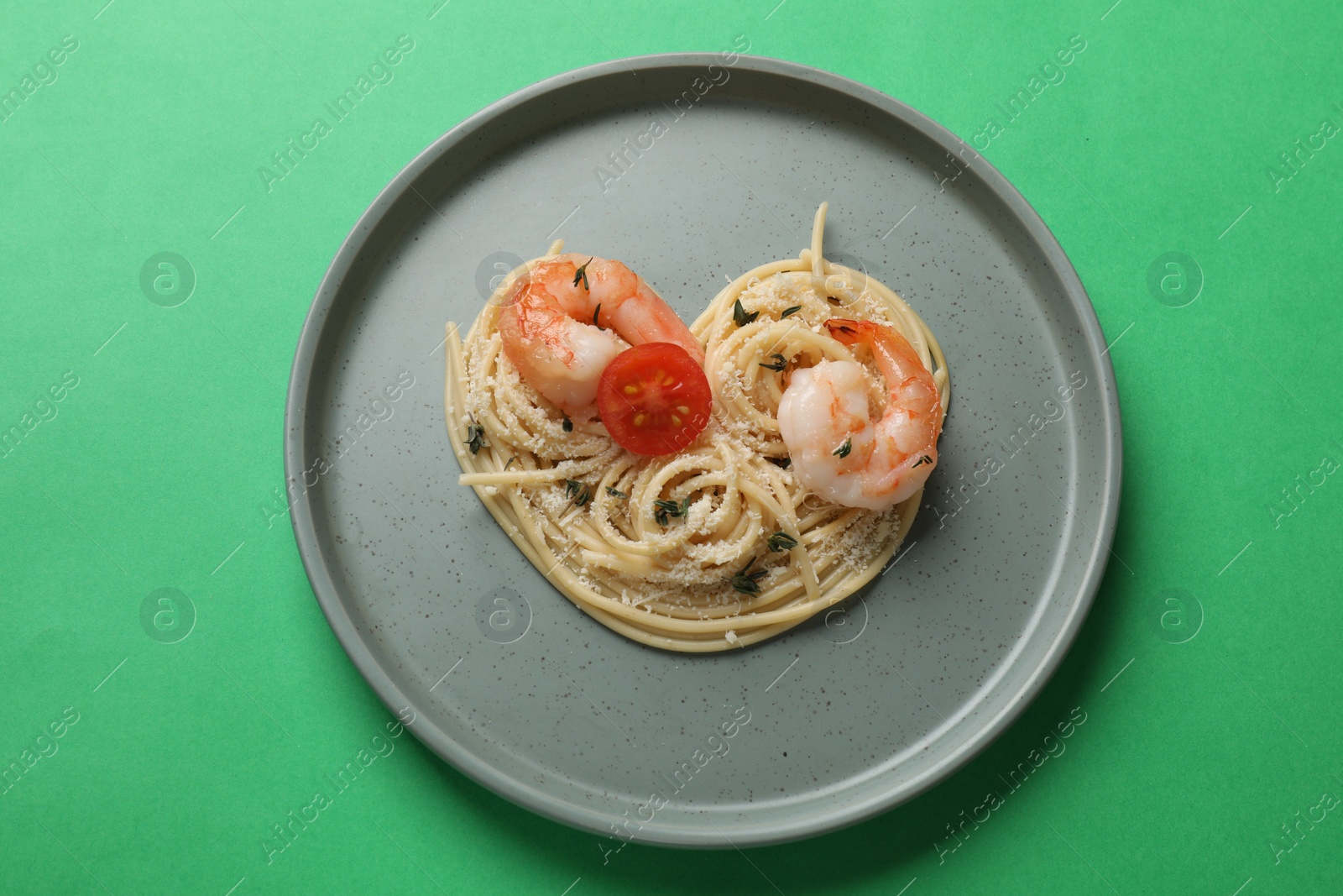 Photo of Heart made of tasty spaghetti, tomato, shrimps and cheese on green background, top view