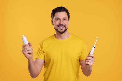 Photo of Happy man holding electric toothbrush and tube of toothpaste on yellow background