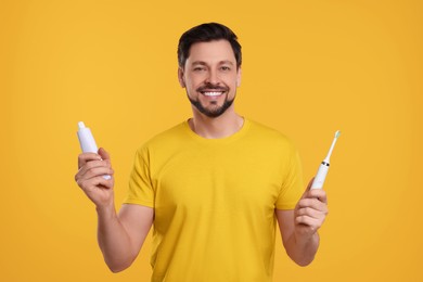 Happy man holding electric toothbrush and tube of toothpaste on yellow background