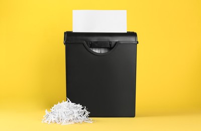 Shredder with sheet of paper and strips on yellow background