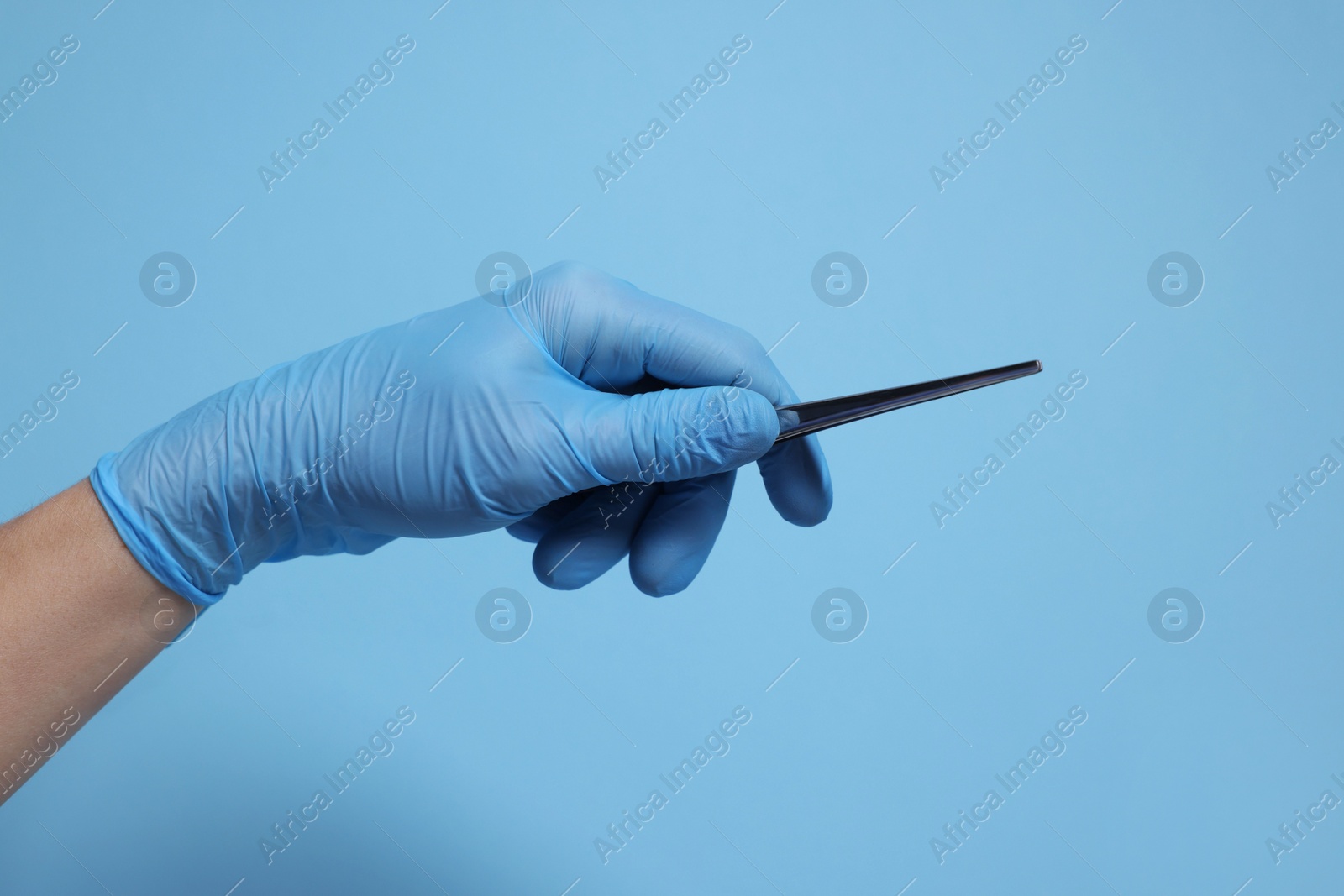 Photo of Doctor wearing medical glove holding tweezers on light blue background, closeup