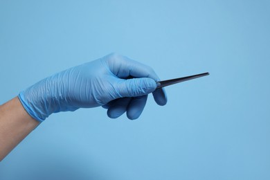 Photo of Doctor wearing medical glove holding tweezers on light blue background, closeup