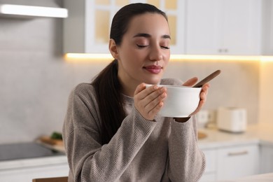 Woman with bowl of tasty soup in kitchen