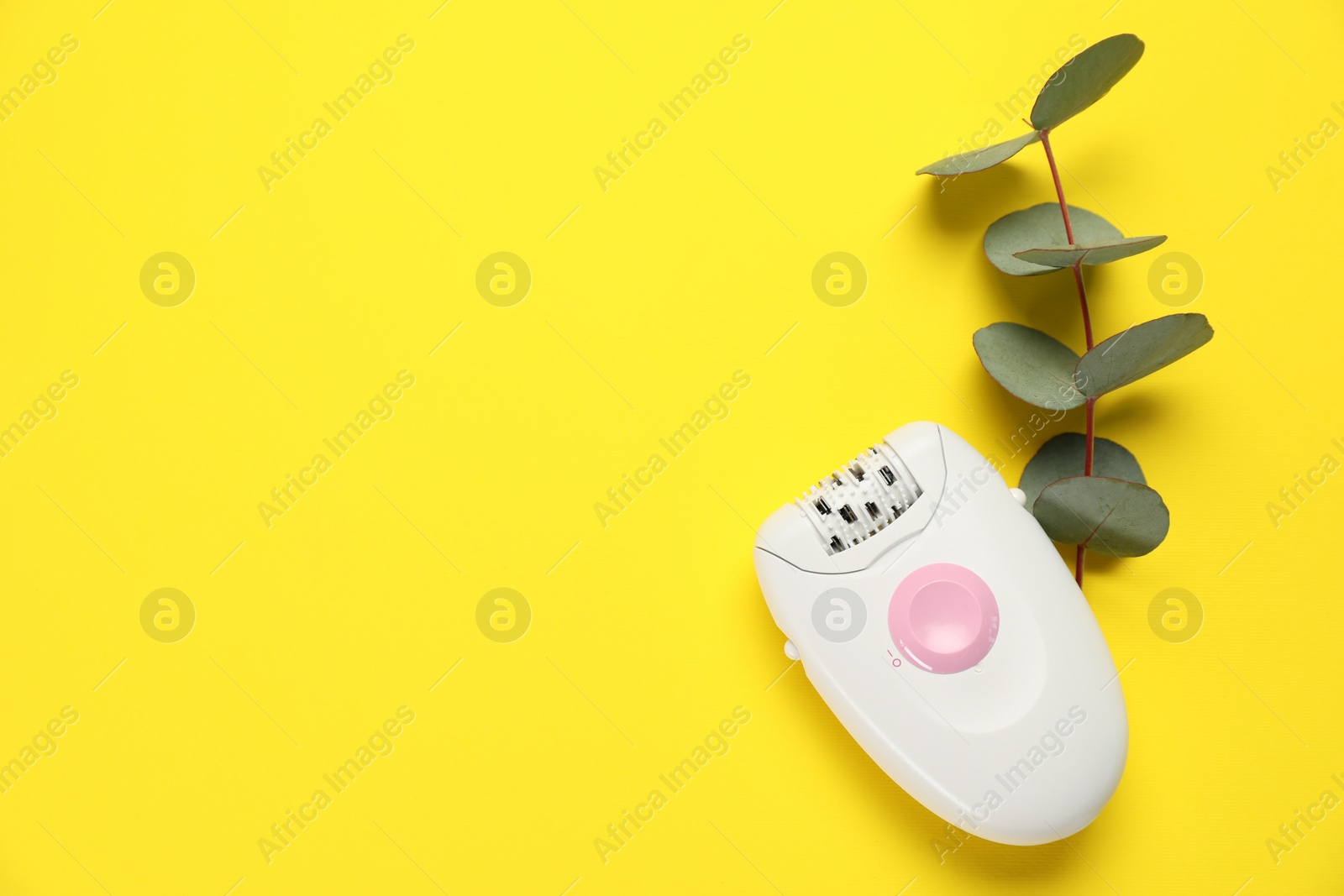 Photo of Modern epilator and eucalyptus branch on yellow background, flat lay. Space for text