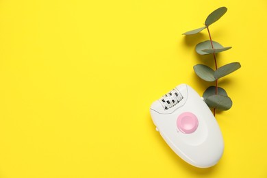 Photo of Modern epilator and eucalyptus branch on yellow background, flat lay. Space for text