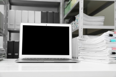 Laptop and documents on desk in office. Space for text