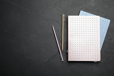 Stylish notebooks and pens on black table, flat lay. Space for text