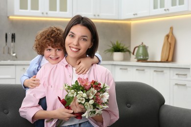 Photo of Little son congratulating his mom with Mother`s day at home, space for text. Woman holding bouquet of beautiful flowers