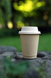Photo of Cardboard takeaway coffee cup with lid on stones outdoors