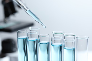 Photo of Dripping liquid from pipette into test tube on blurred background, closeup