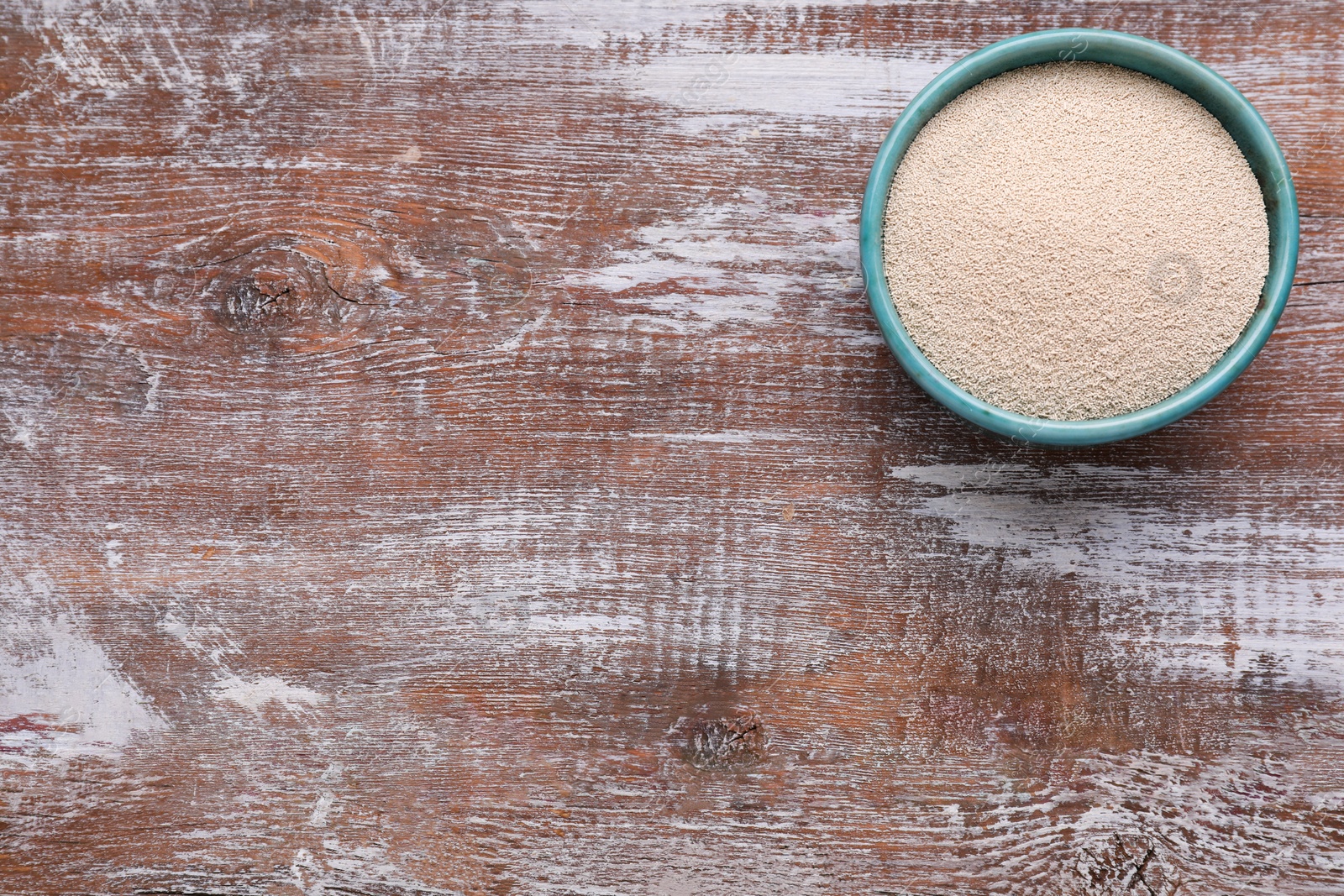 Photo of Bowl of active dry yeast on wooden table, top view. Space for text