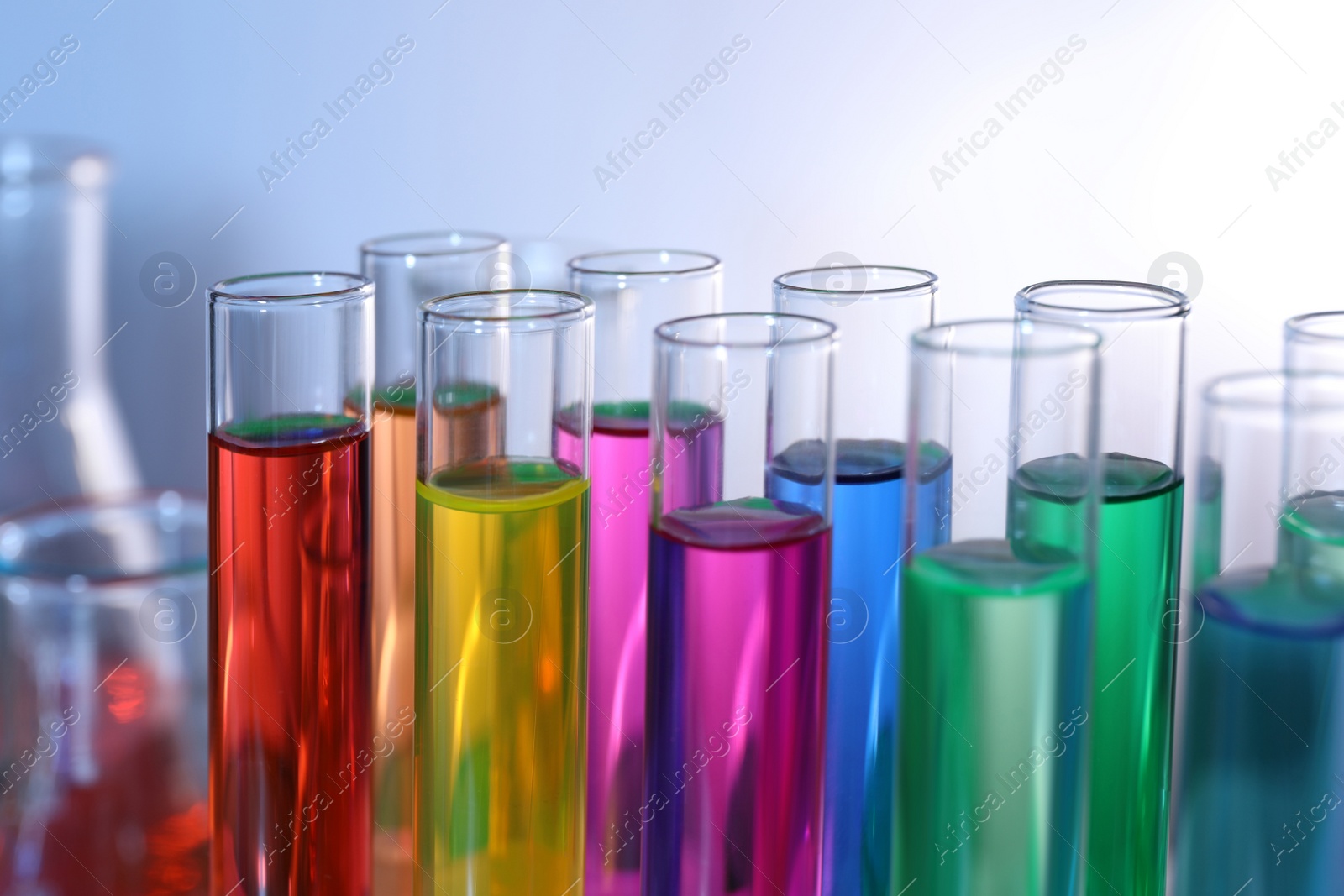 Photo of Many test tubes with colorful liquids on blurred background, closeup