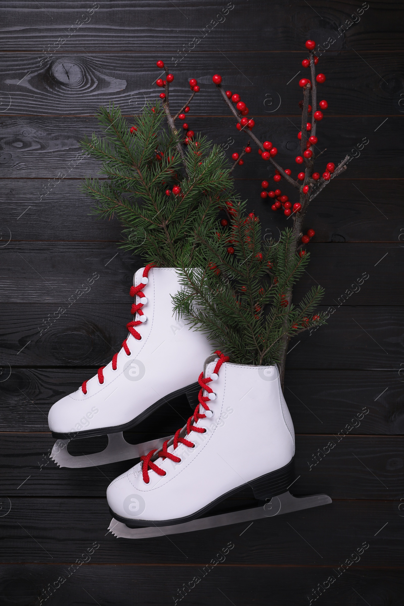 Photo of Pair of ice skates with Christmas decor on black wooden background, flat lay