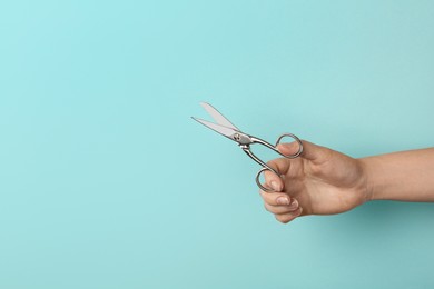 Photo of Woman holding sewing scissors on light blue background, closeup. Space for text