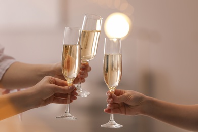 Photo of People clinking glasses of champagne against blurred background, closeup. Bokeh effect