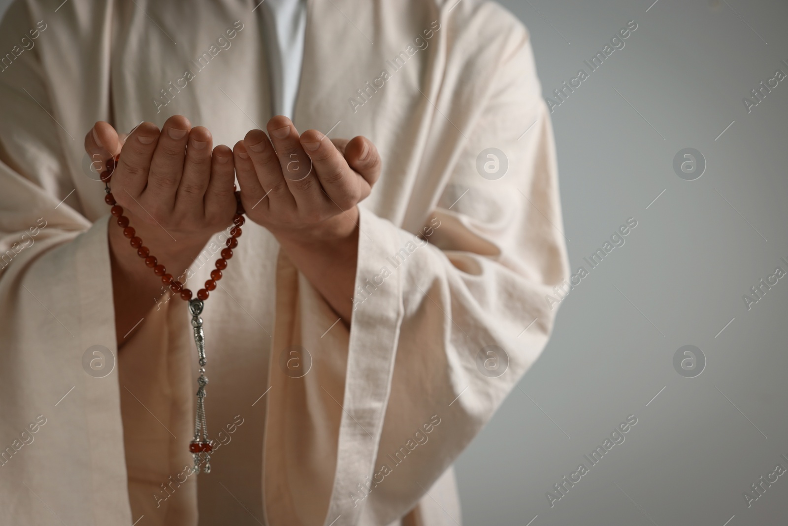 Photo of Muslim man with misbaha praying on light grey background, closeup. Space for text