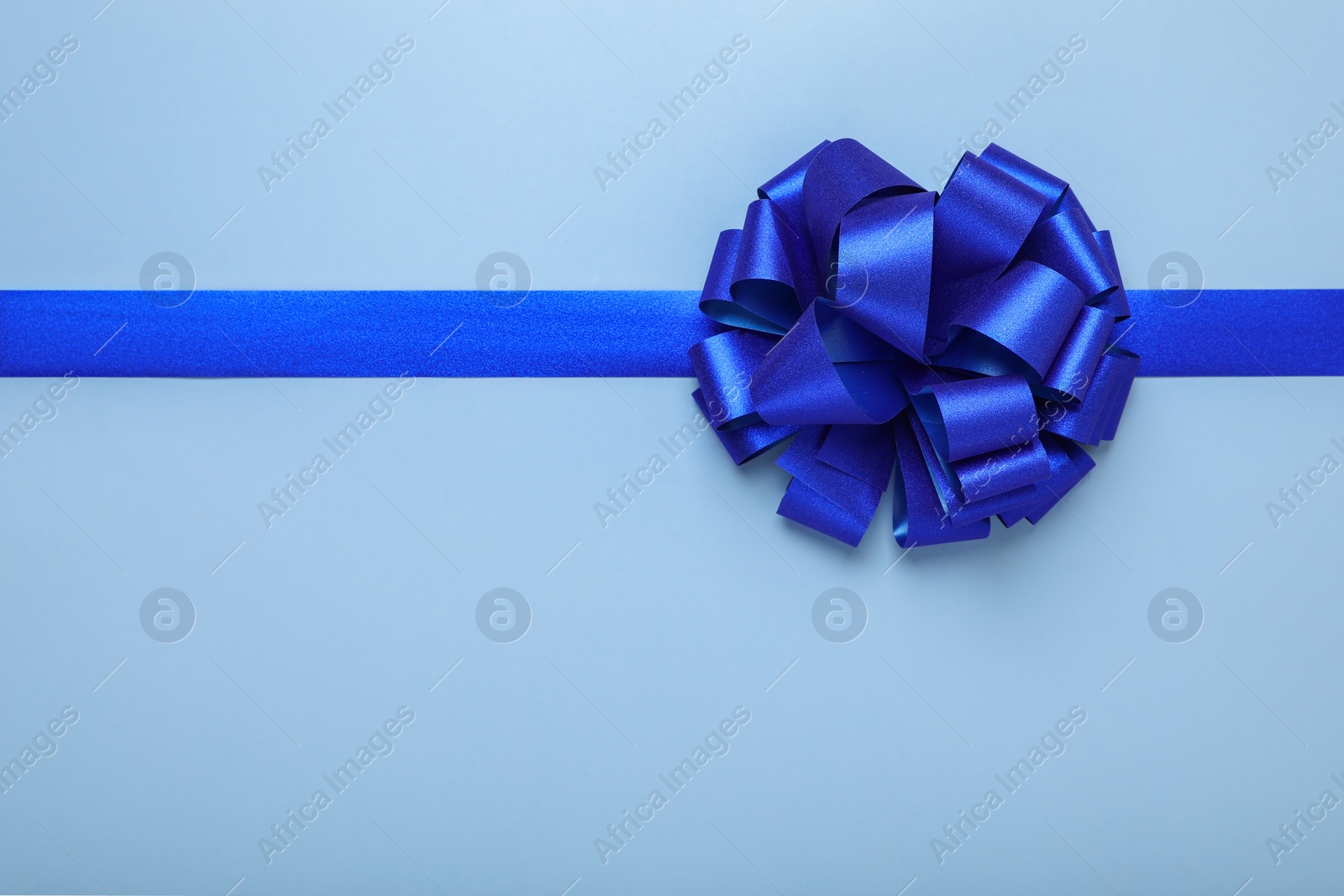 Photo of Ribbon with bow on light blue background, top view. Space for text