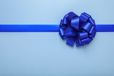 Photo of Ribbon with bow on light blue background, top view. Space for text