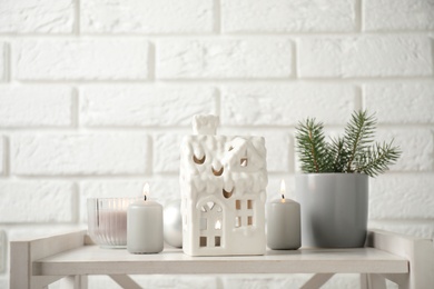 Photo of Composition with house shaped candle holder on white wooden table near brick wall. Christmas decoration