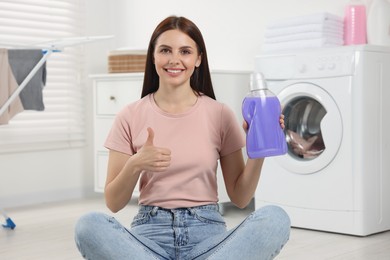 Woman sitting near washing machine and holding fabric softener in bathroom, space for text