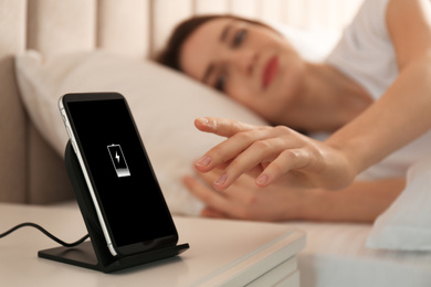 Photo of Woman taking smartphone from wireless charger in bedroom