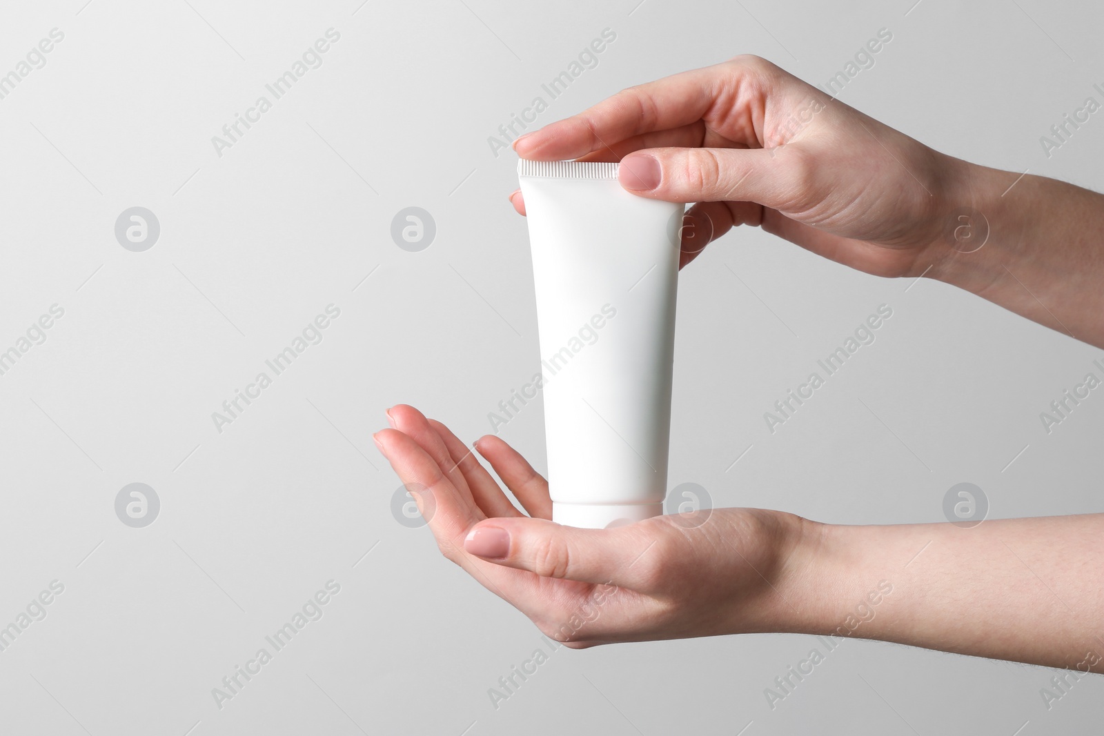 Photo of Woman holding tube of cream on grey background, closeup. Space for text